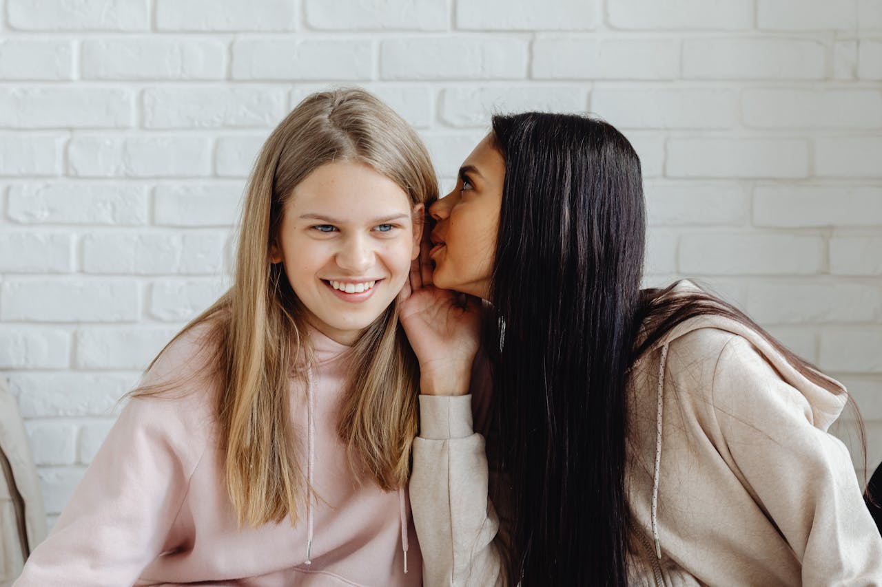 why-choose-us Two teenage girls whispering indoors, sharing secrets and friendship.