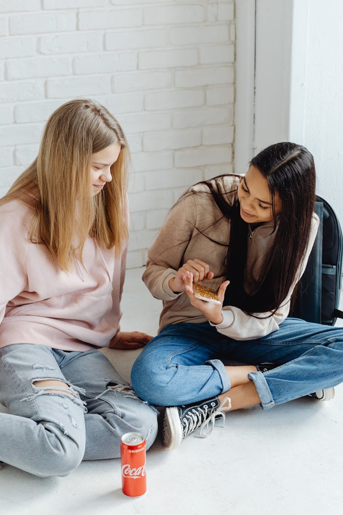 get-in-touch Two teenage girls sit on the floor indoors chatting and snacking.